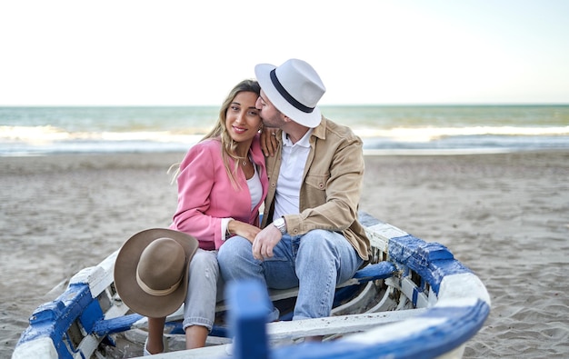Foto pareja joven, enamorado, sentado, en, un, bote, en la playa
