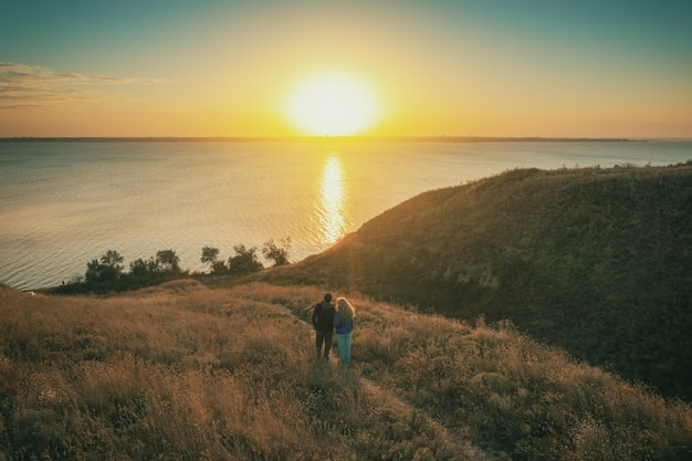 Pareja joven se encuentra en una colina en la noche y mira una hermosa puesta de sol