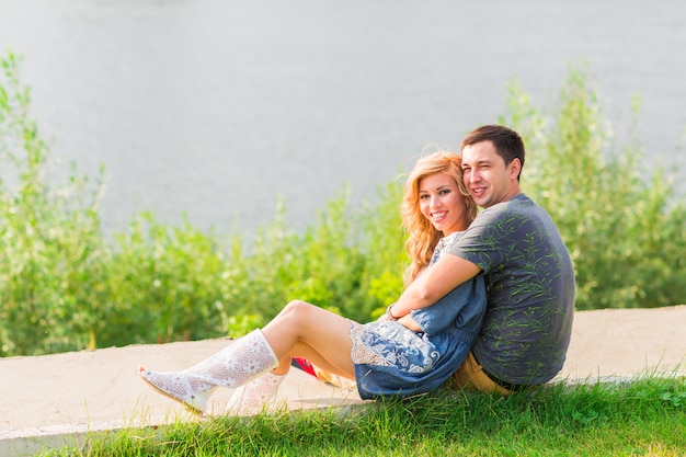 pareja joven es romántica en el parque en un lago. El hombre y la mujer se sientan bajo el sol de verano en la hierba verde.