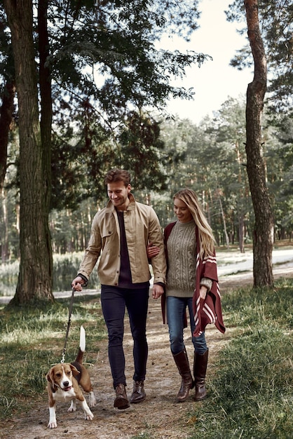 Pareja joven está caminando con perro en el bosque