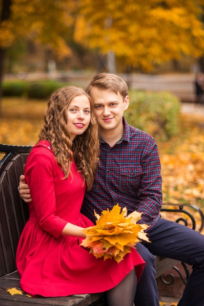 Pareja joven está sentada en un banco de otoño en el parque.