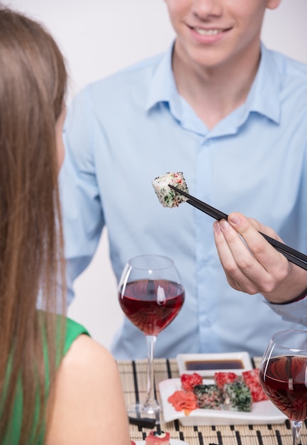 Pareja joven están sentados juntos y comiendo sushi.