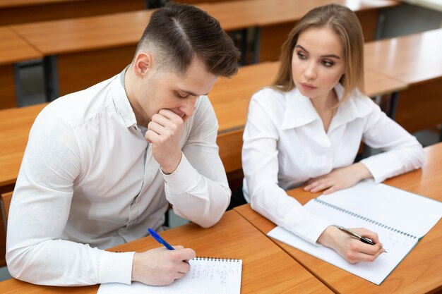 Una pareja joven de estudiantes, un chico y una chica, se sientan en un escritorio en una conferencia y se toman de la mano