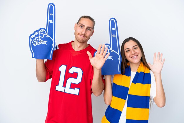 Pareja joven fan de los deportes aislado sobre fondo blanco saludando con la mano con expresión feliz