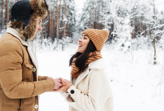 Una pareja joven, feliz y amorosa se abraza en un bosque nevado.