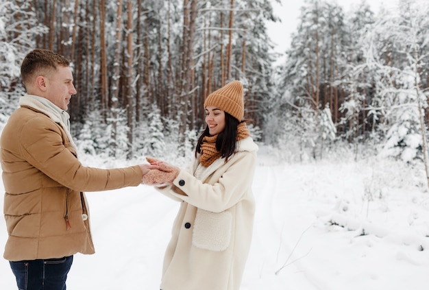 Una pareja joven, feliz y amorosa se abraza en un bosque nevado.