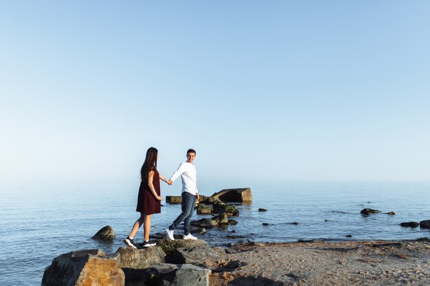 Pareja joven, feliz y amorosa de pie sobre las rocas en el mar, en los brazos y mirándose