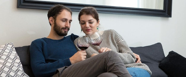 Pareja joven y feliz bebiendo vino y relajándose en casa