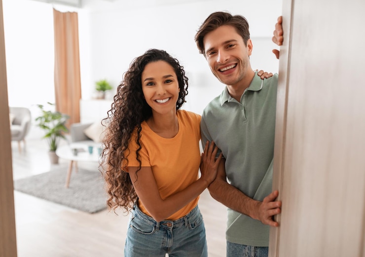 Foto una pareja joven y feliz invitando a la gente a entrar a su casa.