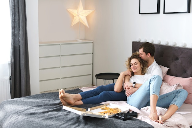 Pareja joven y feliz relajándose en casa. Comer pizza y jugar a la consola de videojuegos.