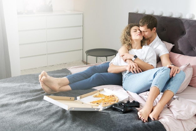 Pareja joven y feliz relajándose en casa. Comer pizza y jugar a la consola de videojuegos.