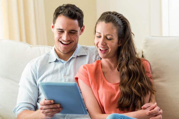 Pareja joven feliz usando tableta digital en el sofá en la sala de estar