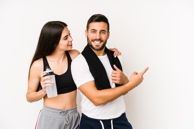 Foto pareja joven de fitness caucásico aislado sonriendo y apuntando a un lado, mostrando algo en el espacio en blanco.