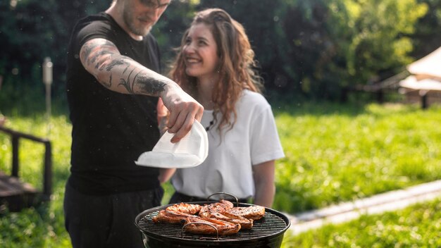 Foto pareja joven friendo carne a la parrilla. verdor alrededor. glamping