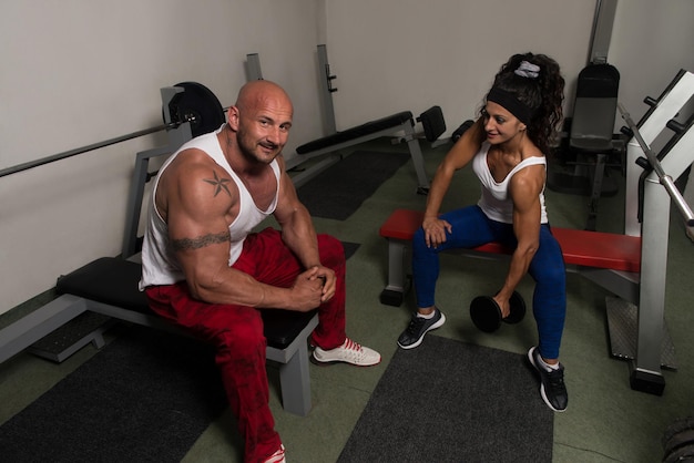 Pareja joven fuerte trabajando con pesas para bíceps en el gimnasio con equipo de ejercicio