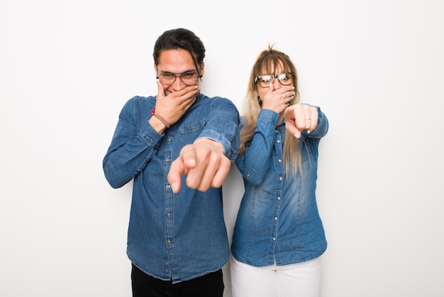 Pareja joven con gafas apuntando con el dedo a alguien y riendo