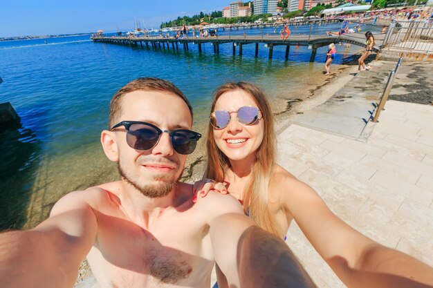 Foto pareja joven con gafas de sol haciendo una foto selfie en el fondo del mar y la ciudad