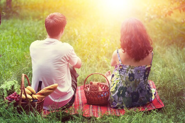 Pareja joven con gatito en una canasta en un picnic sentado de espaldas a la cámara