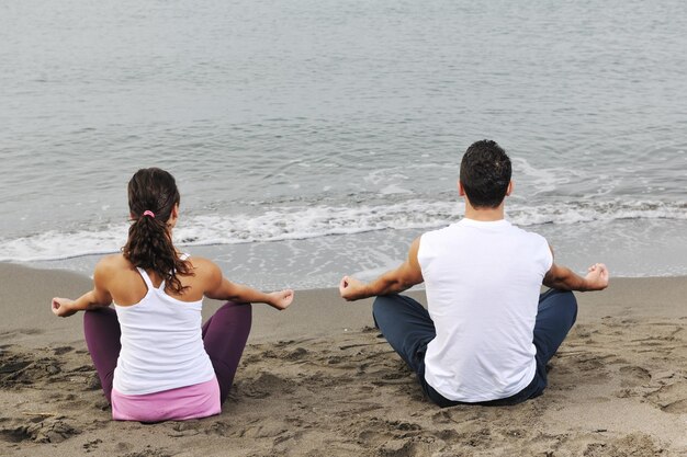 pareja joven gente meditando yoga en posición de loto temprano en la mañana en la playa