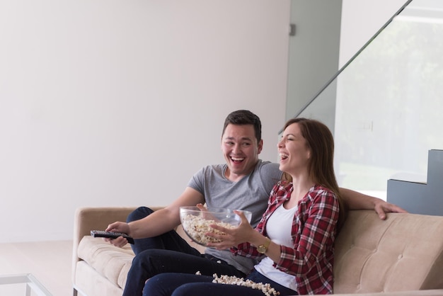 Una pareja joven y guapa que disfruta del tiempo libre viendo la televisión con palomitas de maíz en su villa de lujo