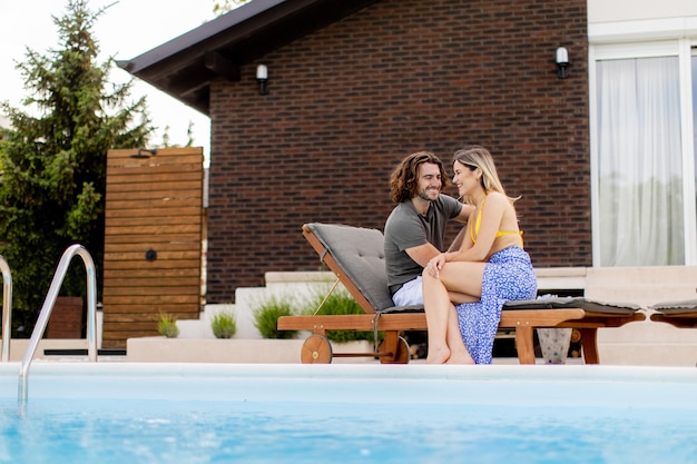 Una pareja joven y guapa se relaja junto a la piscina en el patio trasero de la casa.