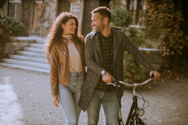 Pareja joven guapo caminando con bicicleta en el parque otoño