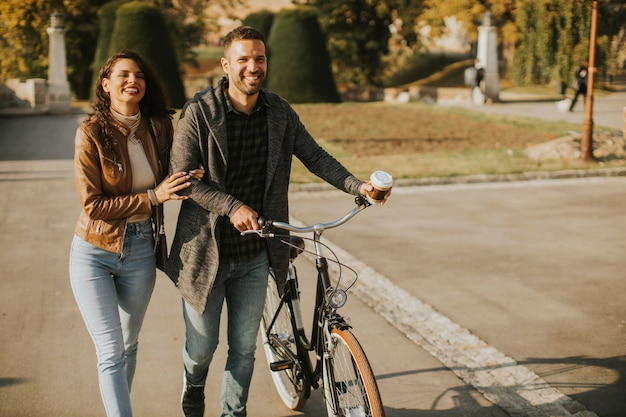 Pareja joven guapo caminando con bicicleta en el parque otoño