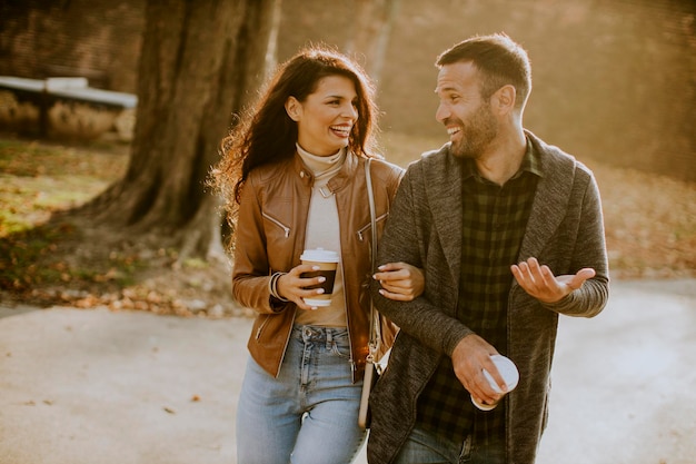 Pareja joven guapo caminando en el parque de otoño con café para llevar tazas en las manos