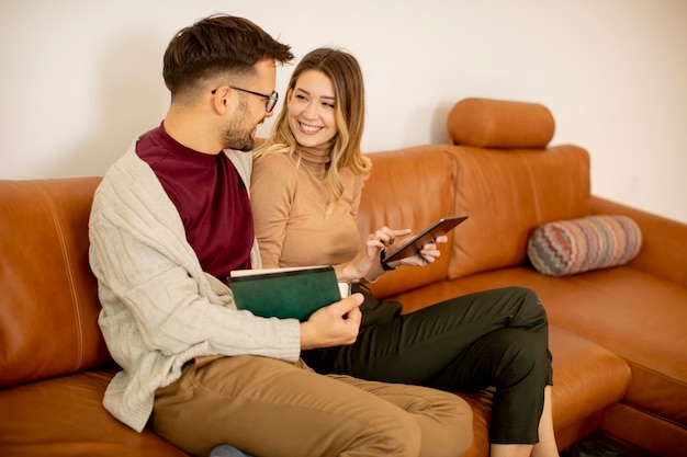 Pareja joven guapo con tableta digital juntos mientras está sentado en el sofá en casa