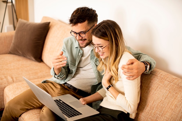 Pareja joven guapo usando laptop juntos mientras está sentado en el sofá en casa