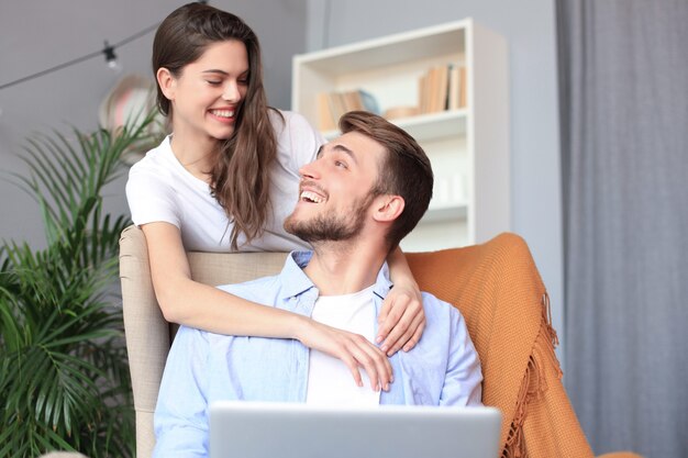 Pareja joven haciendo algunas compras en línea en casa, usando una computadora portátil en el sofá.