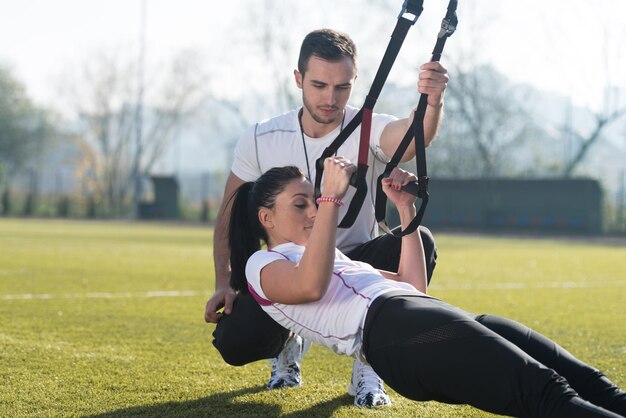 Pareja joven haciendo crossfit con correas de fitness Trx en el área del parque de la ciudad entrenando y haciendo ejercicio para el concepto de estilo de vida saludable de resistencia al aire libre