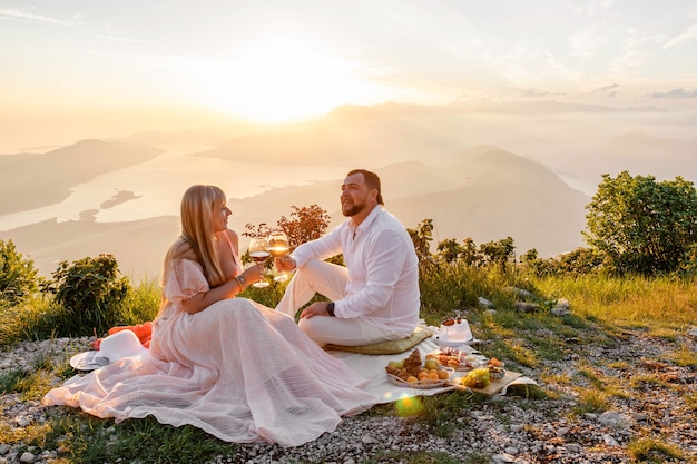 Pareja joven haciendo un picnic al atardecer en las montañas, feliz, riendo