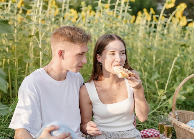 Pareja joven haciendo un picnic en el campo de girasol al atardecer