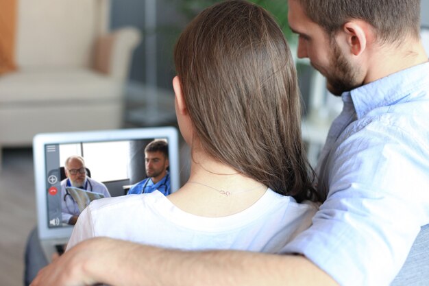 Pareja joven haciendo videoconferencia con médicos en portátil. Coronavirus.