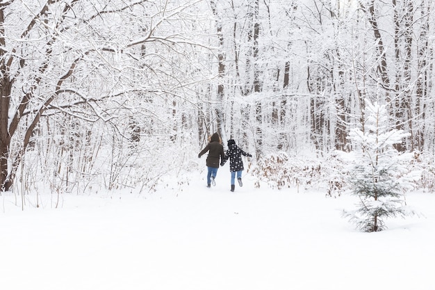 Una pareja joven y hermosa se divierte en el parque cubierto de nieve, corriendo y tomados de la mano. San Valentín