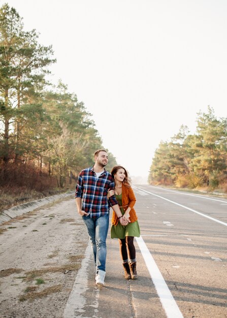 Pareja joven de hombre y mujer sonriendo, caminando al aire libre en una carretera vacía.