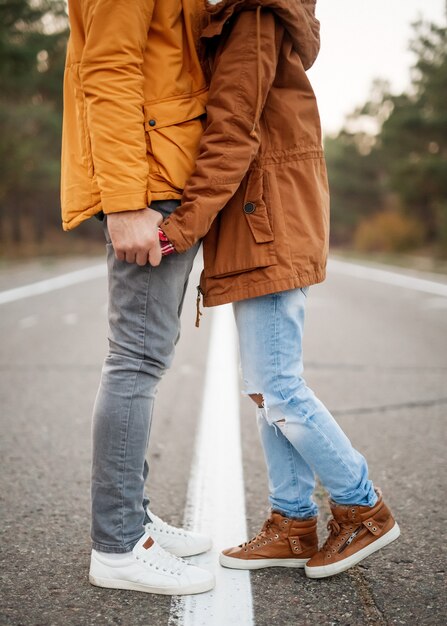 Pareja joven de hombre y mujer, vestidos con ropa de abrigo, tomados de la mano y de pie en medio de una carretera vacía