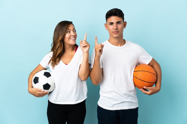 Pareja joven jugando al fútbol y baloncesto en azul con la intención de darse cuenta de la solución mientras levanta un dedo