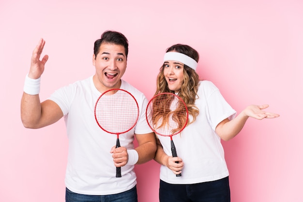 Pareja joven jugando bádminton aislado recibiendo una agradable sorpresa, emocionado y levantando las manos.