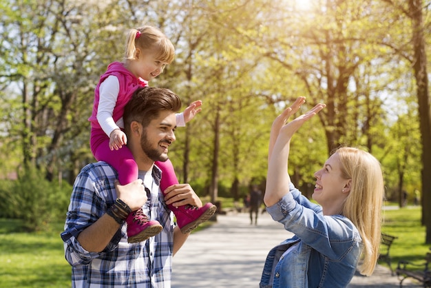 Pareja joven jugando y divirtiéndose con su adorable hija en un parque en un día soleado