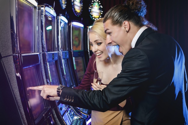 Pareja joven jugando máquinas tragamonedas en el casino