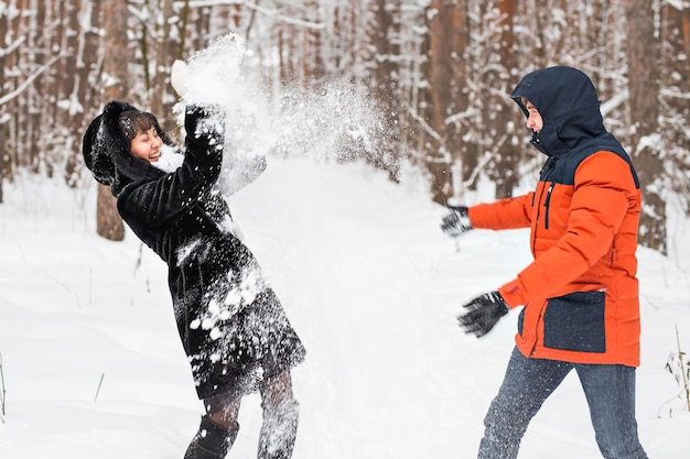 Pareja joven jugando en la nieve, luchando con bolas de nieve.