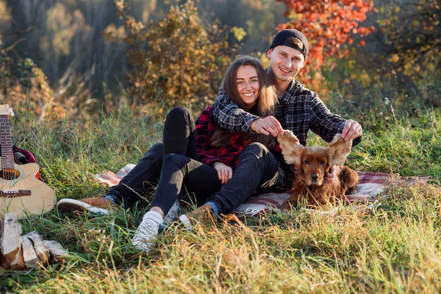 Pareja joven jugando con su perro mascota de picnic en el parque.