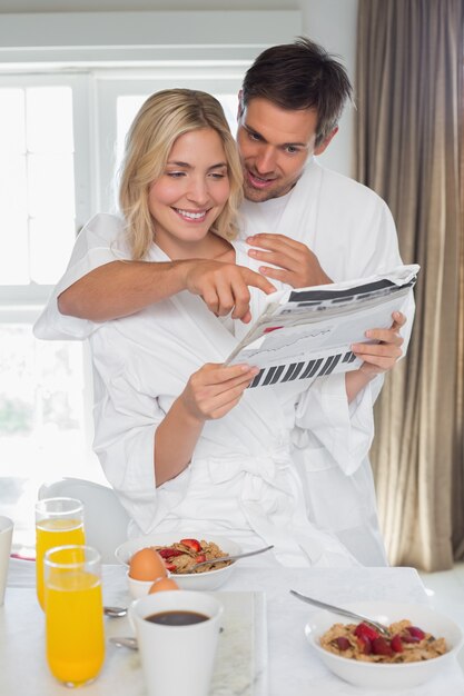 Pareja joven leyendo el periódico mientras desayuna en casa