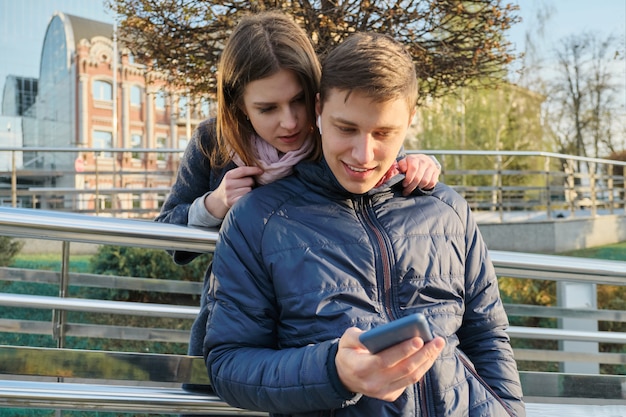 Pareja joven leyendo el texto en el teléfono, el fondo de la ciudad de primavera