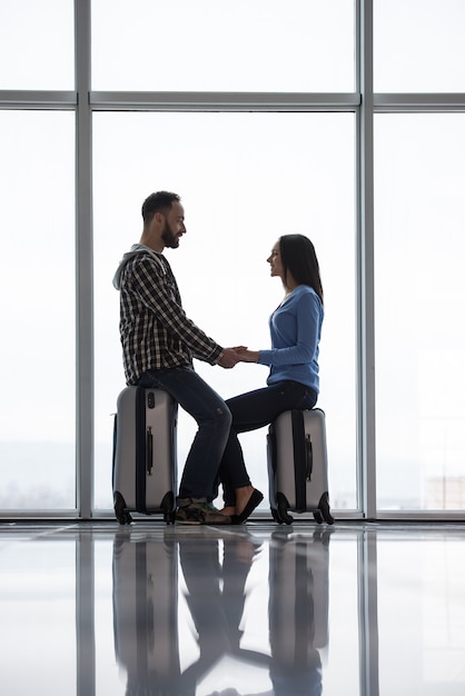 Pareja joven con maletas cerca de la ventana panorámica.