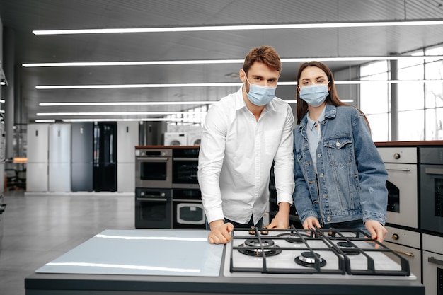 Pareja joven en máscaras médicas mirando electrodomésticos de cocina en un centro comercial