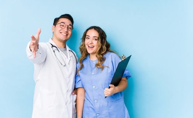 Pareja joven médico posando sobre fondo azul aislado se siente seguro dando un abrazo