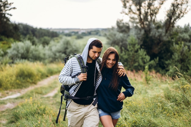 Pareja joven con mochilas en la espalda en el bosque. Hombre cariñoso besa a su bella novia en una caminata en el bosque